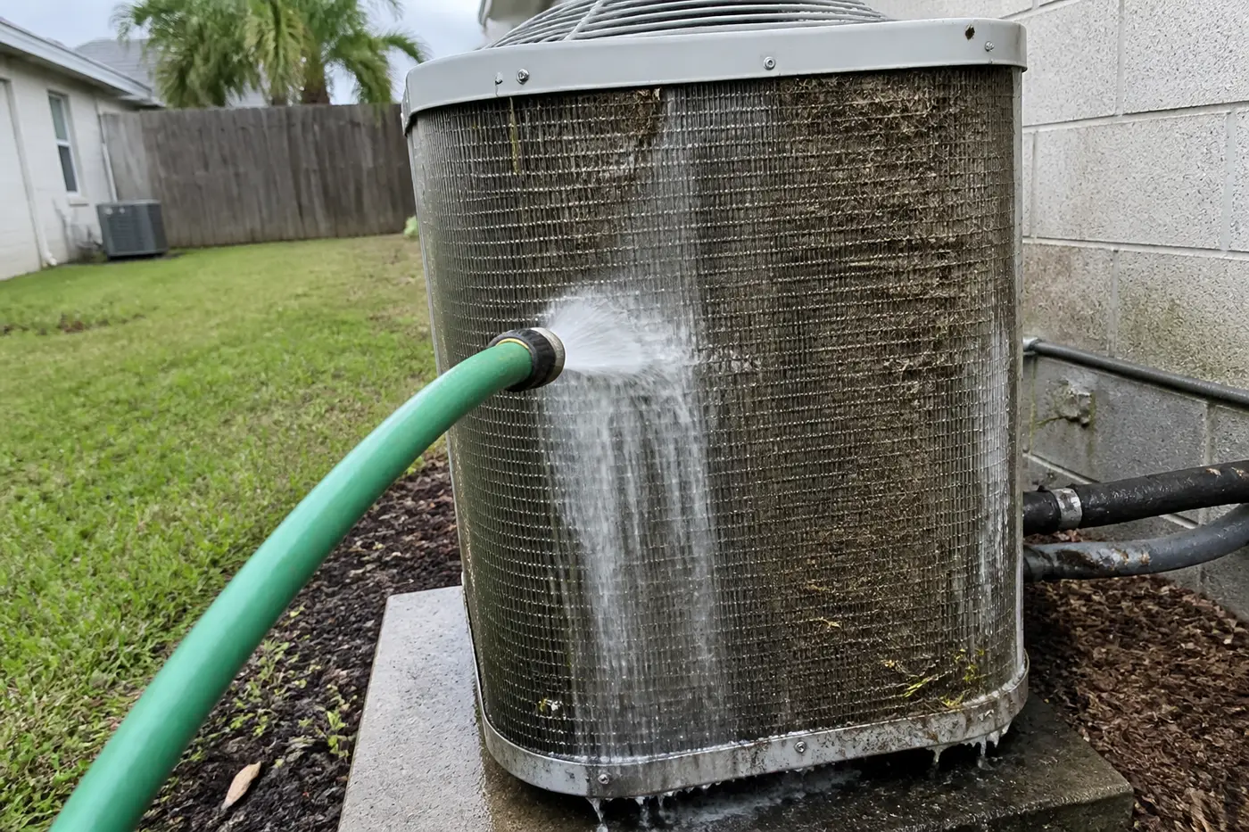 Dirty outdoor condenser fins being rinsed with a garden hose in a Florida backyard