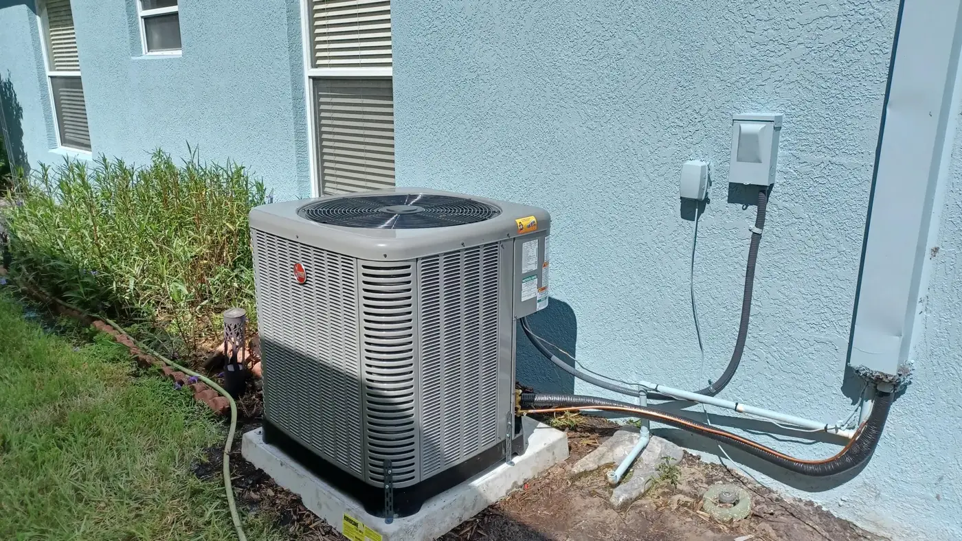 Rheem outdoor condenser on a pad beside a blue stucco wall on Alan Jones's heat pump job