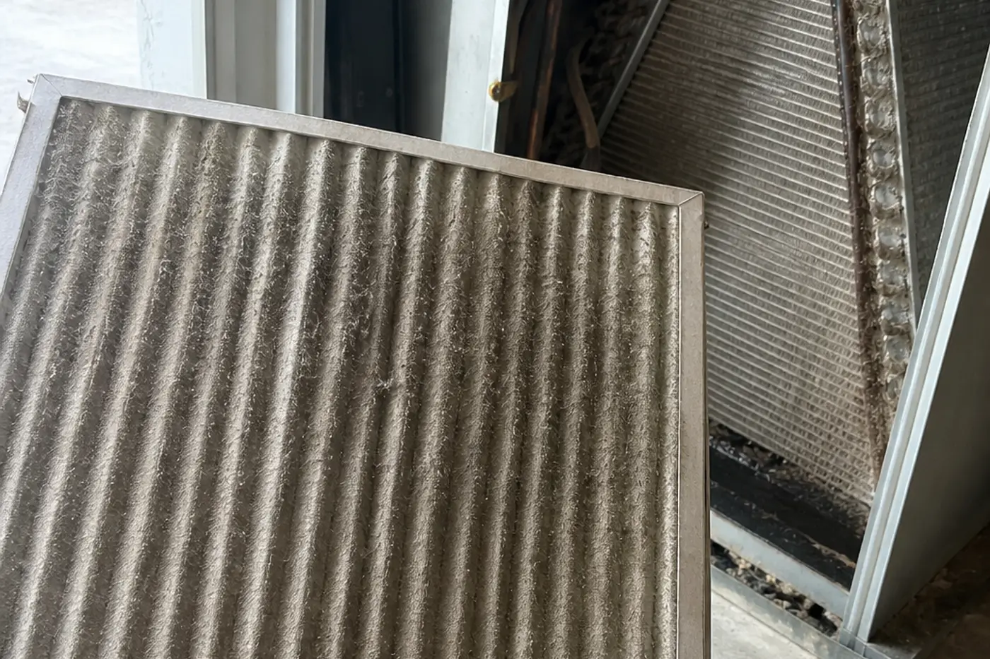 Dirty pleated air filter held next to an open air handler where the evaporator coil sits