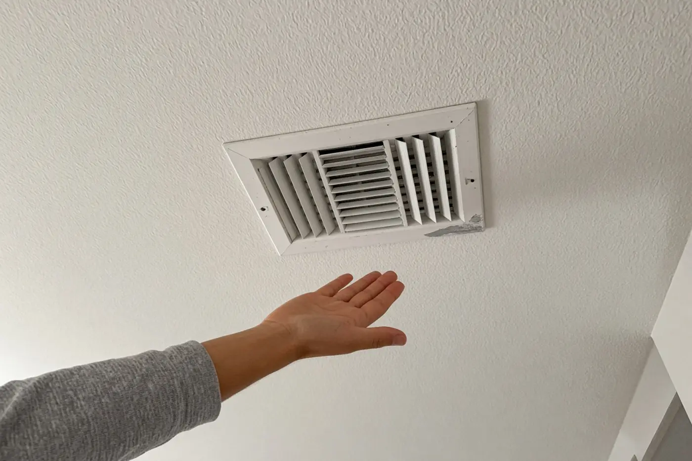 Hand checking a ceiling supply vent during a Wesley Chapel heat test